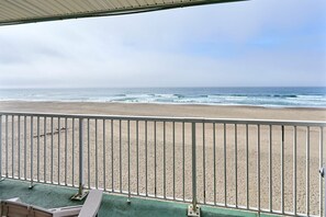 A beach view from a balcony with a metal railing, a green floor, and a clear sky. - Fireplace Suite With King Bed, Full Kitchen, Ocean Views - Heated Indoor Pool and Hot Tub! (Lincoln City)