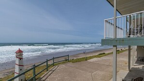 A coastal view with a lighthouse, a concrete walkway, and a covered seating area overlooking the beach.