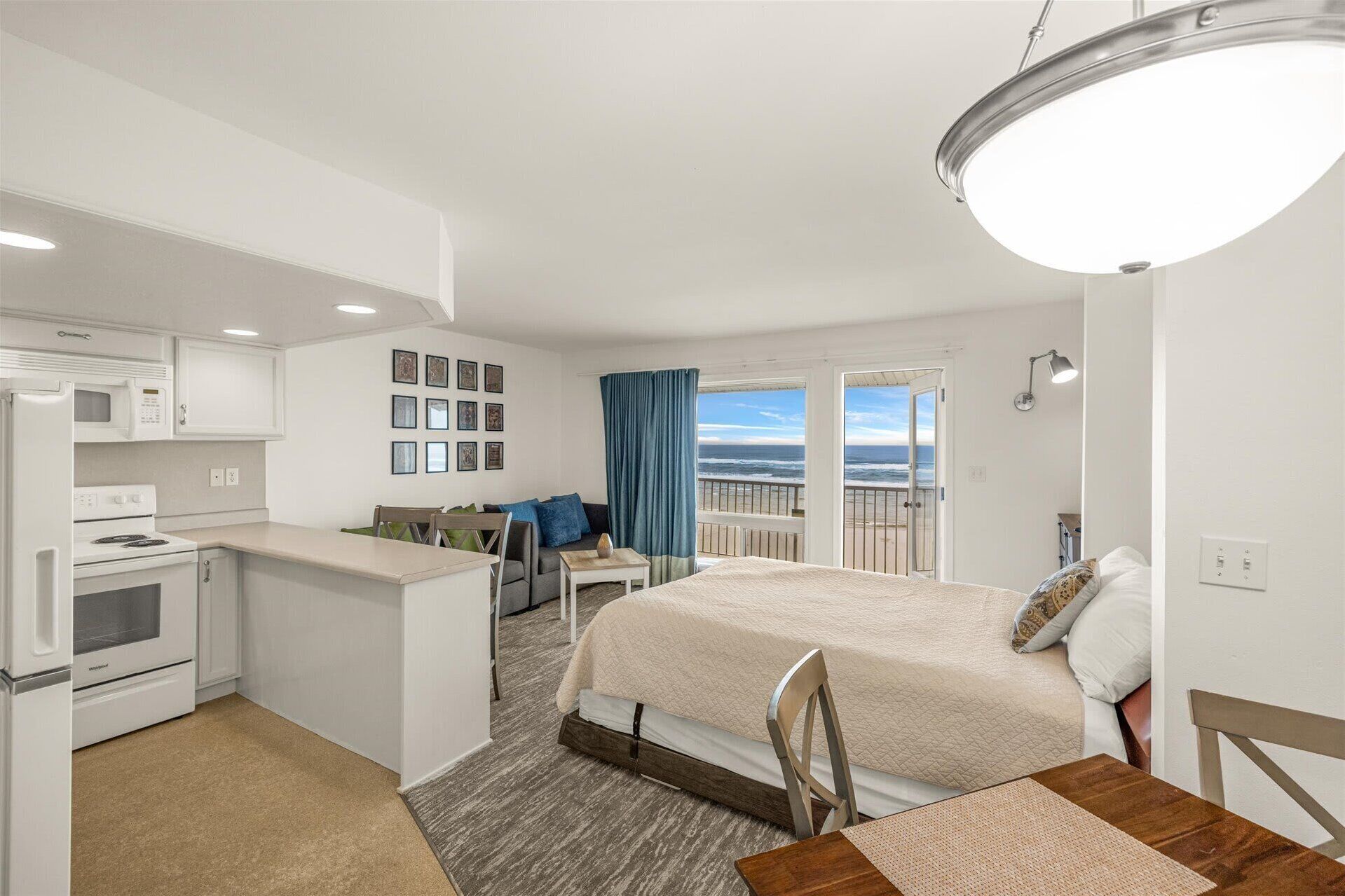 A compact hotel room with a kitchenette, a bed, a dining area, and a balcony with a view.