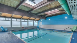 Une piscine intérieure avec de grandes fenêtres, des chaises bleues et vertes, et un mur bleu et blanc.