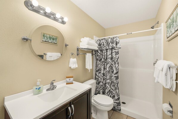 A bathroom with a sink, toilet, shower, and a mirror with lights.