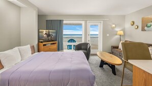 Une chambre d’hôtel comprenant un lit, un bureau avec une télévision, une chaise, une petite table et un balcon avec vue sur l’océan.