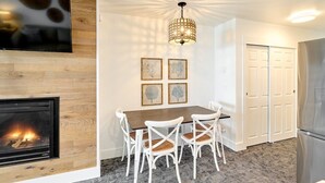 A modern kitchen with a built-in fireplace, white chairs, a wooden dining table, and a ceiling light fixture.