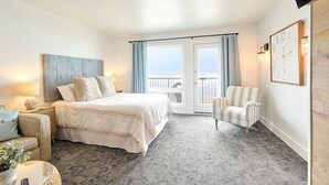 A hotel room with a bed, a chair, a small table, a balcony with curtains, and a clock on the wall.