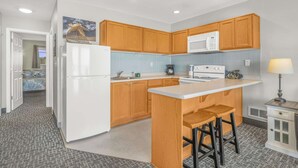 Cocina compacta con armarios de madera, un refrigerador blanco, un microondas y una pequeña isla con taburetes.