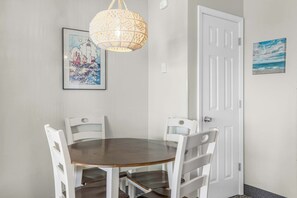 Un coin repas avec une table ronde et quatre chaises blanches, un luminaire suspendu au design original et deux œuvres d’art encadrées accrochées aux murs.
