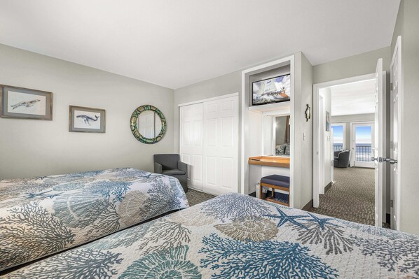 Habitación de hotel con dos camas, televisión, escritorio y vista a la playa.