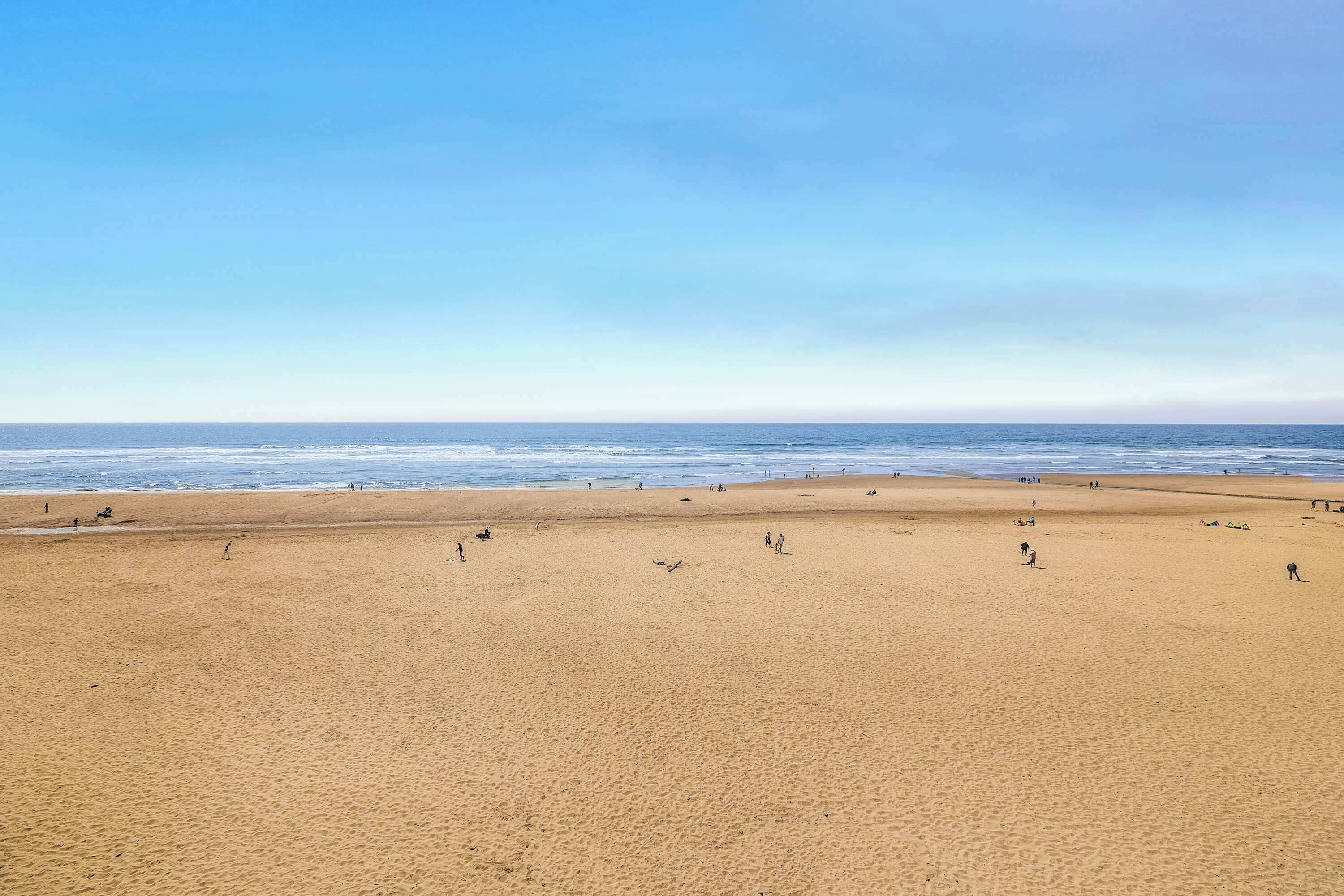 Een breed zandstrand met verspreide mensen, een heldere lucht en de oceaan op de achtergrond.