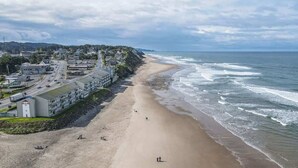 Un pueblo costero con playa de arena, una carretera que bordea la costa y edificios de arquitectura industrial.
