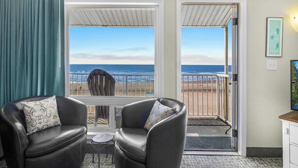 Habitación con vista a la playa, que incluye dos sillones de cuero con cojines estampados, una mesita y una puerta que da al exterior.