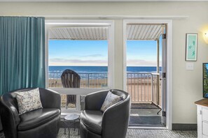 Habitación con vista a la playa, que incluye dos sillones de cuero con cojines estampados, una mesita y una puerta que da al exterior.