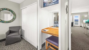 Un pasillo con un sillón gris, un escritorio de madera con una banca, un cuadro enmarcado de un velero y una puerta blanca.