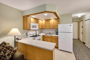 Cocina compacta con muebles de madera, un microondas, una estufa, un refrigerador y una encimera.