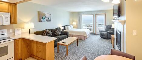 A hotel room with a kitchenette, a sofa, a bed, a dining area, and a balcony with a view.