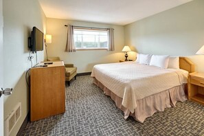 Une chambre d’hôtel comprenant un lit, une table de chevet, une lampe, une télévision et un bureau avec une chaise.