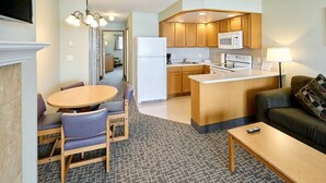 Een ruimtelijk ingerichte zithoek met een kitchenette, een eethoek met een ronde tafel en stoelen, een bank en een salontafel.
