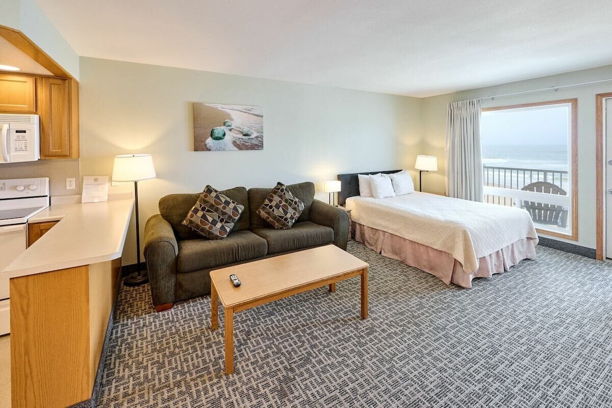 A hotel room with a kitchenette, a sofa, a bed, a small table, and a view of the ocean.