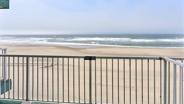 Uitzicht op het strand vanaf een balkon met een metalen hekwerk, een heldere lucht en de oceaan op de achtergrond.
