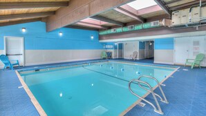 An indoor swimming pool with clear water, blue tiled walls, and a wooden ceiling. - Oceanfront Suite - King Bed - Heated Indoor Pool & Hot Tub (Lincoln City)