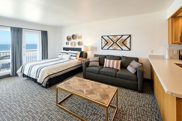 Habitación de hotel con cama, sofá, mesa de centro y vista al océano.