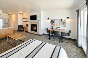 A hotel room with a bed, a small table, a fireplace, a TV, and artwork on the wall.