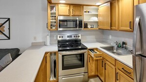A compact kitchen with wooden cabinets, a stainless steel refrigerator, a microwave, a stove, and a built-in oven. - Oceanfront Suite - King Bed - Heated Indoor Pool & Hot Tub (Lincoln City)
