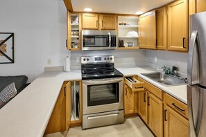 Cocina compacta con armarios de madera, refrigerador de acero inoxidable, microondas, estufa y horno empotrado.