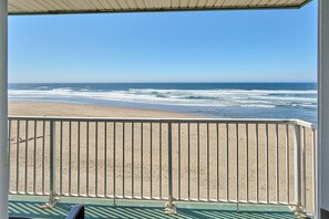 Vista a la playa desde un balcón con barandilla, cielo despejado y olas del océano.