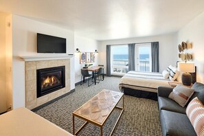 A hotel room with a fireplace, a television, a bed with a view of the sea, a sofa, and a dining area.