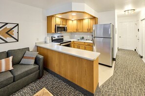 A compact kitchen with wooden cabinets, a stainless steel refrigerator, and a built-in microwave.