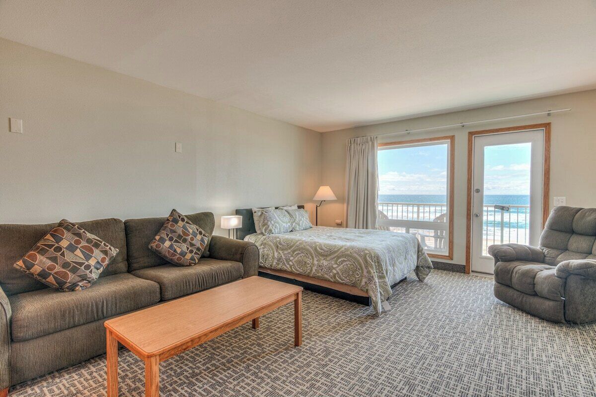 Quarto de hotel com cama, sofá, poltrona e vista para o mar.