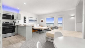A compact hotel room with a kitchenette, a bed with a view, a small dining table, and a balcony with a view. - Corner King Suite, Stunning Ocean and River Views! (Lincoln City)