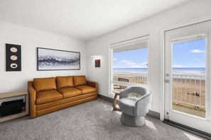 Una sala de estar moderna con un sofá de cuero marrón, un sillón gris, una mesita y un ventanal con vista a la playa.