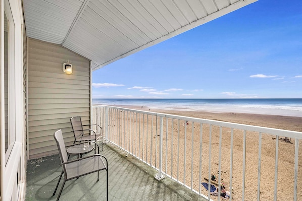 A balcony with a view of the beach, metal chairs, and a small table.