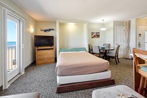 A hotel room with a bed, a television, a dining table with chairs, a balcony with a view, and a door. - King Suite - Oceanfront Balcony & Central Location - Pool & Hot Tub! (Lincoln City)