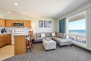 A modern living room with a sofa, ottoman, and a dining area with chairs and a table. - King Suite - Oceanfront Balcony & Central Location - Pool & Hot Tub! (Lincoln City)