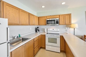 A kitchen with wooden cabinets, a microwave, a stove, and a sink. - King Suite - Oceanfront Balcony & Central Location - Pool & Hot Tub! (Lincoln City)