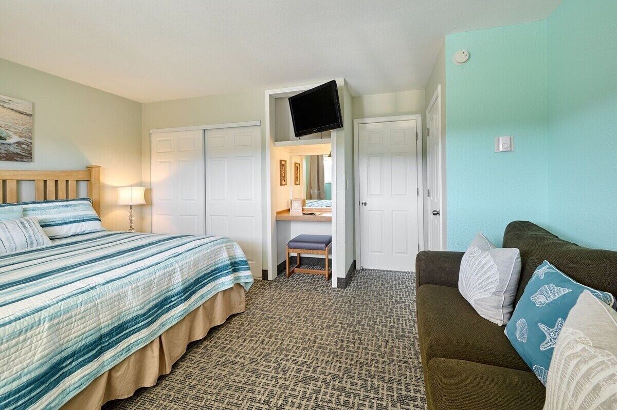 Een hotelkamer met een bed, een sofa, een aan de muur bevestigde televisie en een deur naar een badkamer.