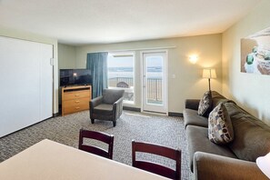 A hotel room with a balcony, a television, a dining table, and a sofa.