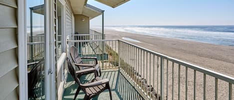 Een balkon met uitzicht op het strand, een hekwerk en twee stoelen.