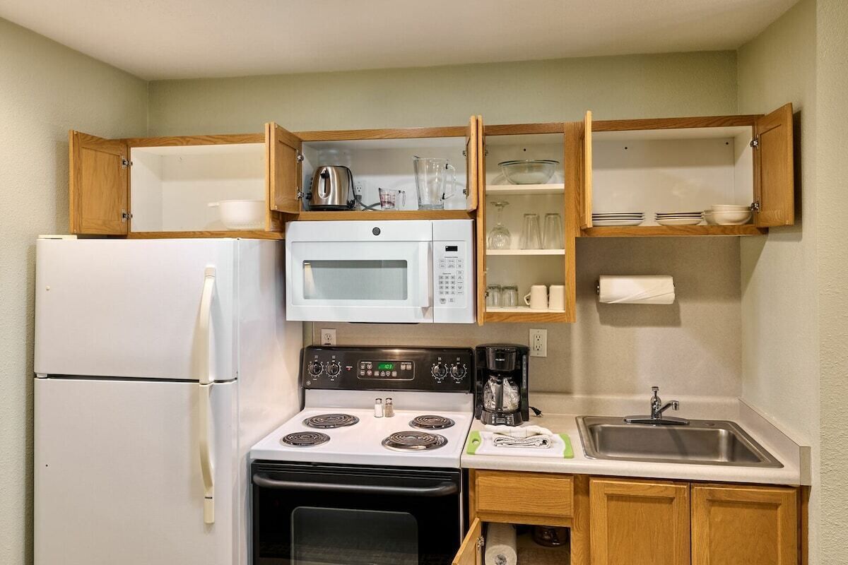 A compact kitchen with a refrigerator, microwave, stove, and a sink.