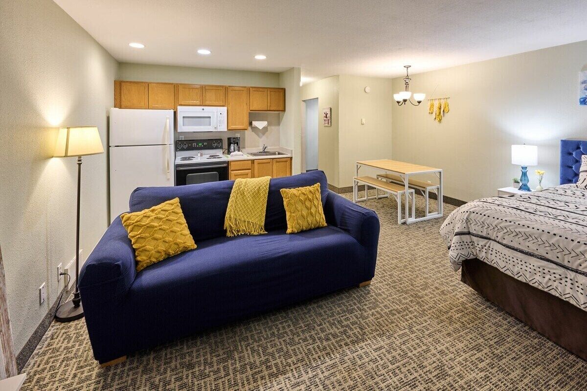 A compact hotel room with a sofa, a bed, a kitchenette, and a dining table.