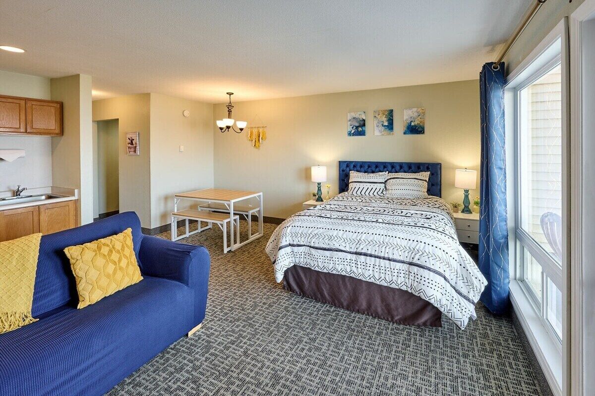 A hotel room with a bed, a sofa, a small table, and a window with curtains.