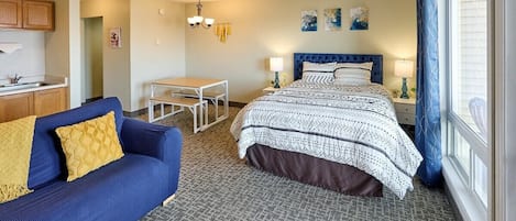 A hotel room with a bed, a sofa, a small table, and a window with curtains.