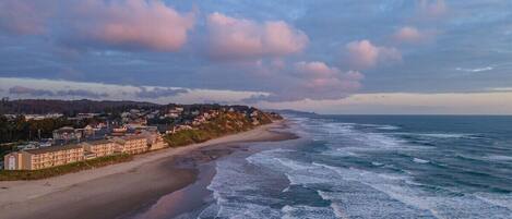 A coastal town with a beachfront hotel, ocean waves, and a cloudy sky.