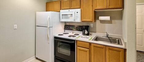 A compact kitchen with a refrigerator, microwave, stove, oven, and a sink.