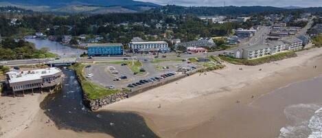 Luftaufnahme einer Küstenstadt mit Strand, Parkplatz und Gebäuden, darunter ein blaues Hotel.