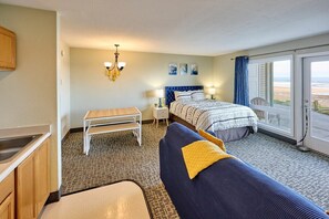 A bedroom with a bed, bedside tables, a desk, and a view of the beach through a sliding door.