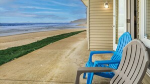 A beachfront property with a concrete pathway leading to a porch with blue chairs.