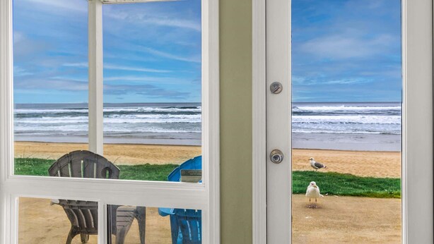 A view of the ocean through a door with a chair and umbrella inside.